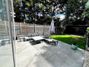 A patio with a table and chairs, a white umbrella, and a wooden fence. - Architect-Designed Luxury Retreat, 3BR Chessington (Chessington)