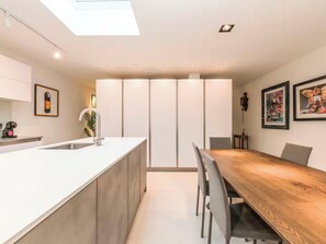 A modern kitchen with a central island, a dining area with a wooden table, recessed ceiling lights, and artwork on the walls. - Architect-Designed Luxury Retreat, 3BR Chessington (Chessington)