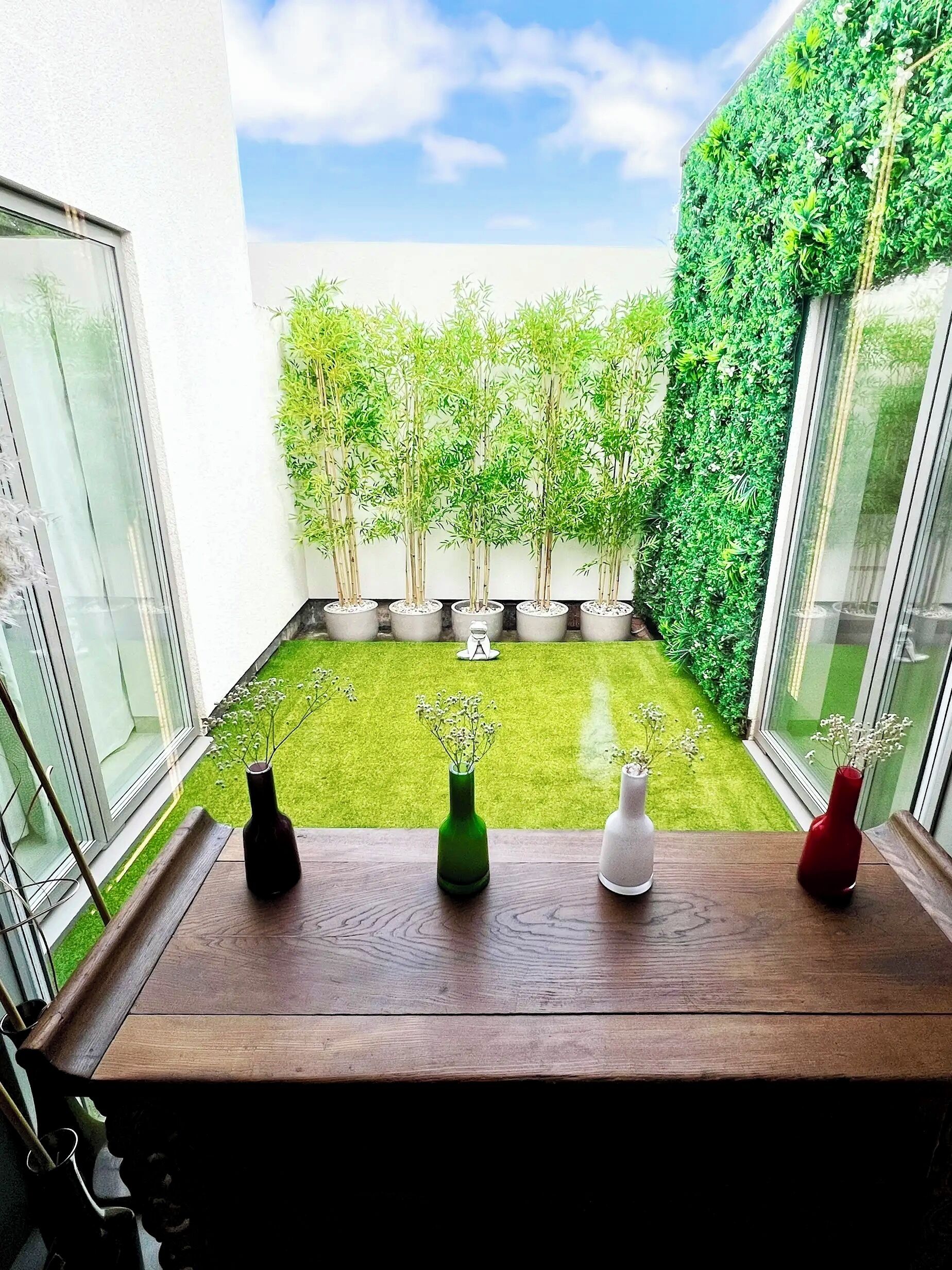 A view from a window overlooking a small courtyard with artificial grass, potted plants, and a green wall.