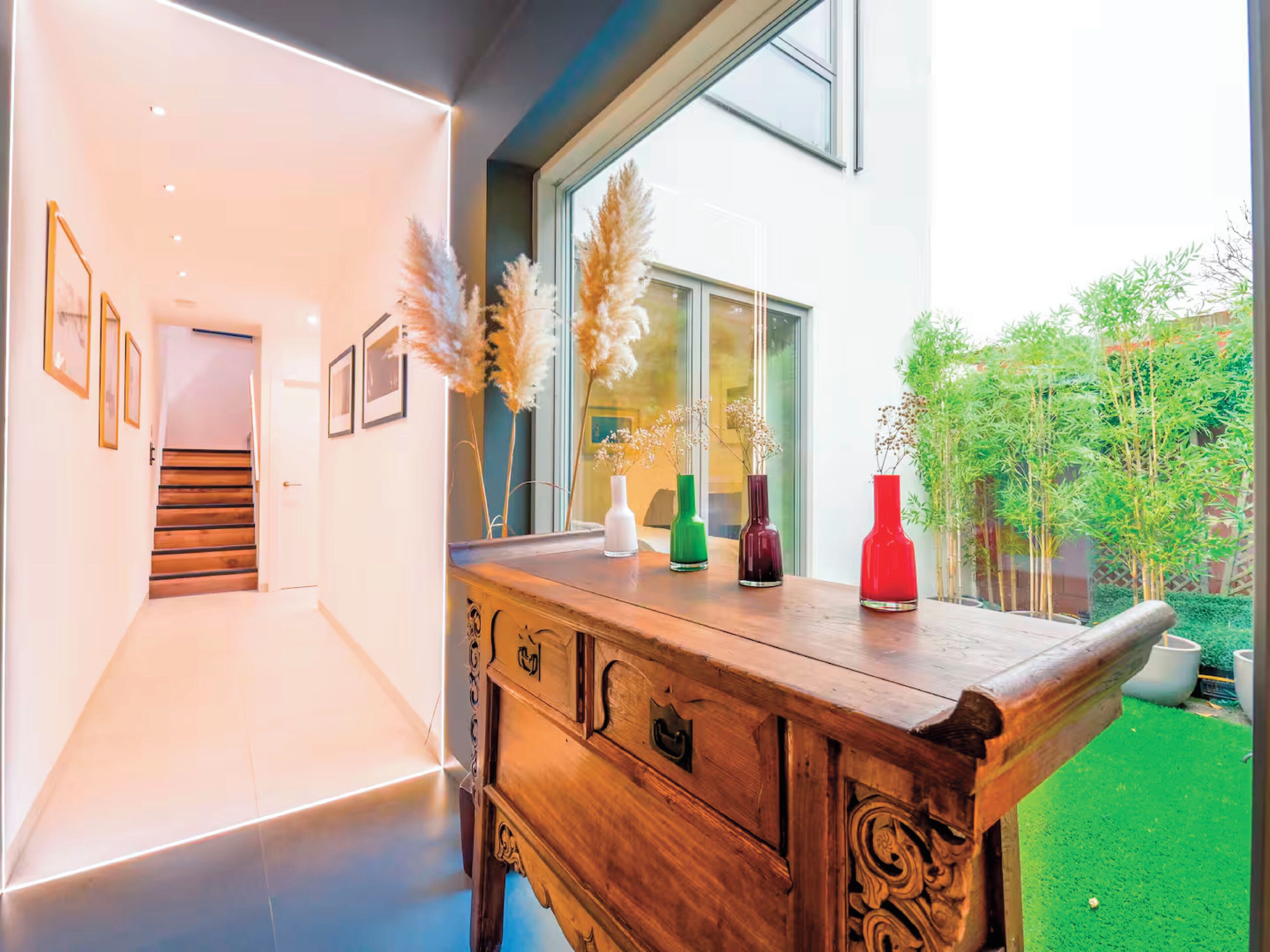 A modern interior with a wooden bench, framed pictures on the wall, and a view of the outside.
