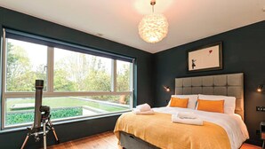 Ein Schlafzimmer mit großem Fenster, einem Teleskop, einem Bett mit orangefarbenen Kissen und einem gerahmten Bild an der Wand.