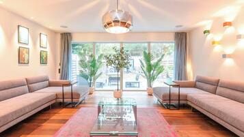 A modern living room with a glass coffee table, two sofas, a large window, and a hanging light fixture.