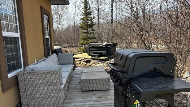 A deck with outdoor furniture, a grill, and a television. - Charming  Rustic cabin w/Jacuzzi at Fowler Lake, SK (Loon Lake No. 561)