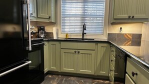 A kitchen with green cabinets, a black refrigerator, a window with blinds, and a tiled backsplash. - Charming  Rustic cabin w/Jacuzzi at Fowler Lake, SK (Loon Lake No. 561)