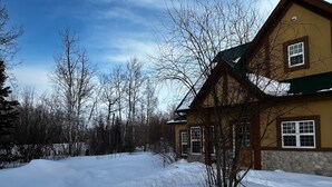 A house with a snow-covered yard and leafless trees. - Charming  Rustic cabin w/Jacuzzi at Fowler Lake, SK (Loon Lake No. 561)
