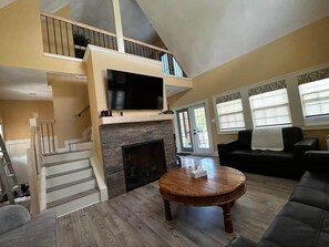 A spacious living area with a fireplace, a staircase, a flat-screen TV, and a cozy seating arrangement.
