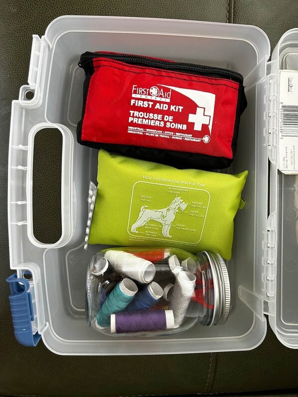 A first aid kit, a green cloth, and spools of thread in a clear plastic case.