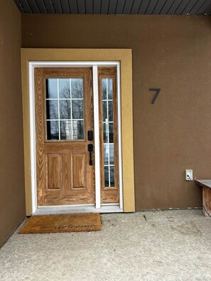 A wooden front door with a glass panel, a doormat, and a mailbox on the wall.