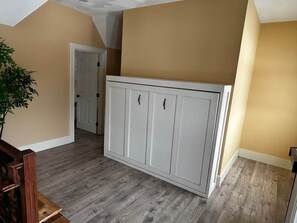 Une pièce dotée d’une grande armoire blanche, d’un plancher en bois et de murs de couleur beige.