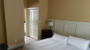 Ein Schlafzimmer mit Bett, Nachttisch, Lampe und einer Tür zu einem anderen Raum.