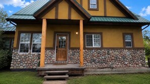Une maison à deux étages, avec des fondations en pierre, un toit végétalisé et un porche à l’avant avec des marches.