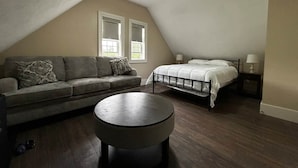 Une chambre avec un plafond en pente, un lit, un canapé, une table basse ronde et deux lampes de chevet.