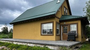 Une maison à deux étages avec un toit en métal vert, une terrasse en bois et un barbecue.