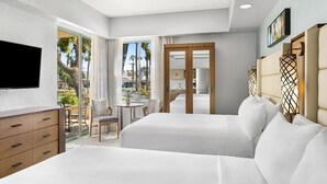 Ein Hotelzimmer mit zwei Betten, einem Fernseher, einem Schreibtisch und einem Balkon mit Blick auf Palmen.