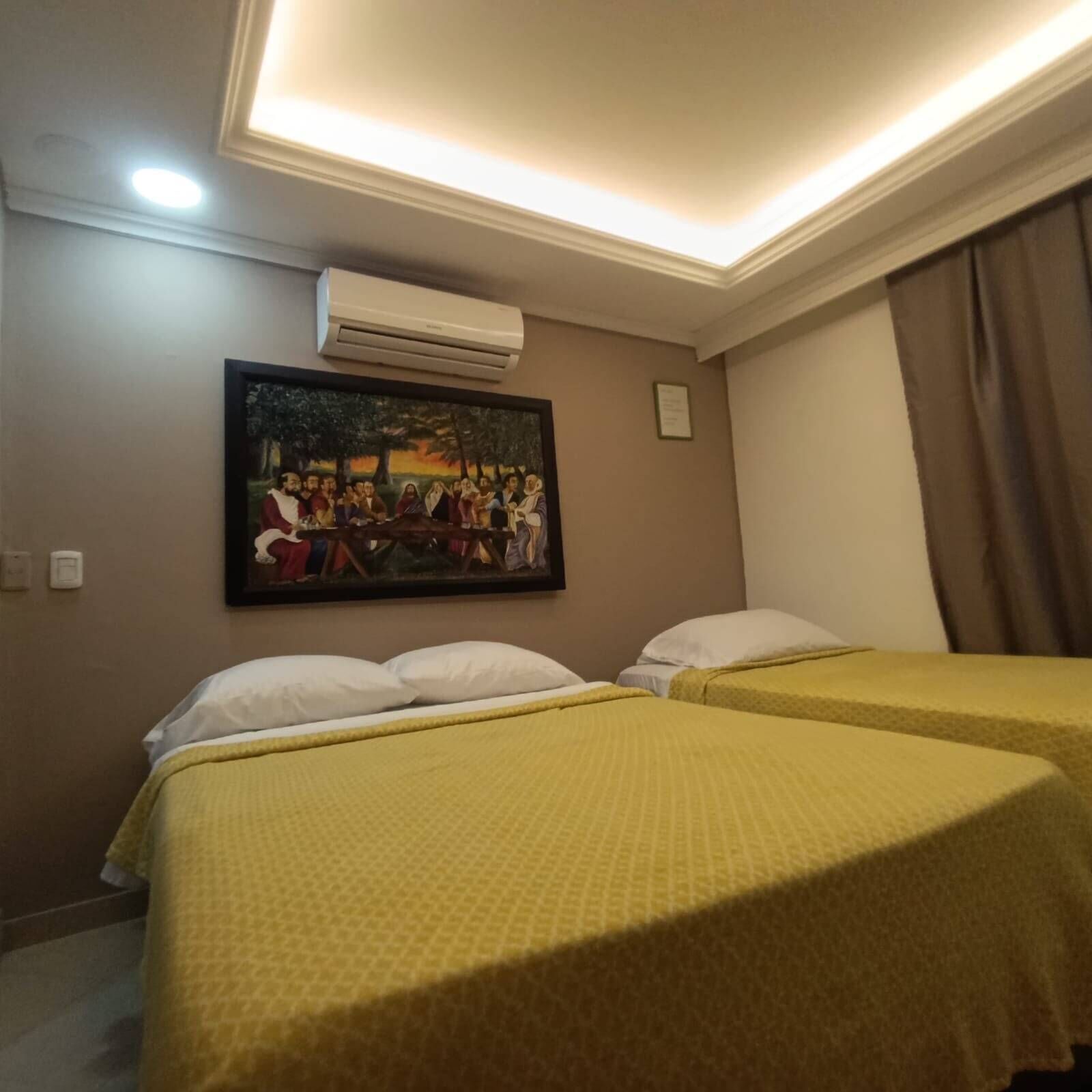 Une chambre d’hôtel avec deux lits, un tableau au mur, un appareil de climatisation et une fenêtre avec des rideaux.