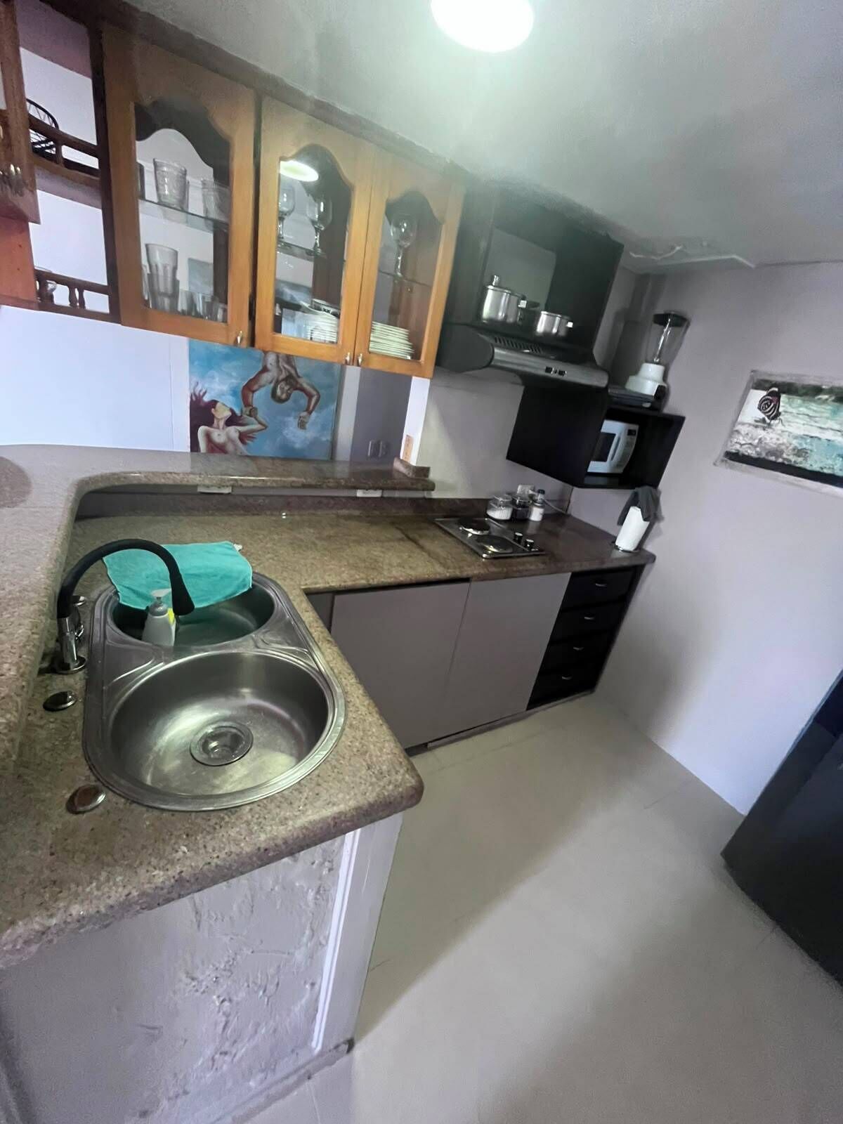 A kitchen with a granite countertop, stainless steel sink, wooden cabinets, a microwave, and a blender.