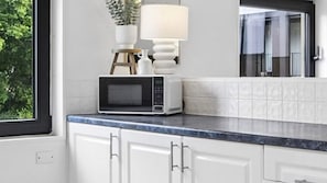 A kitchen with white cabinets, a microwave, a small wooden stool, and a potted plant. - Sandy Calm, Manly Walk to Beach, Corso & Ferry (Manly)