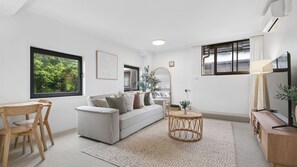 A modern living room with a sofa, chairs, a round coffee table, and a TV. - Sandy Calm, Manly Walk to Beach, Corso & Ferry (Manly)