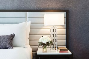 Ein ordentlich bezogenes Bett mit Kissen und einem Nachttisch mit Lampe, einer Vase mit Blumen und einem Buch.