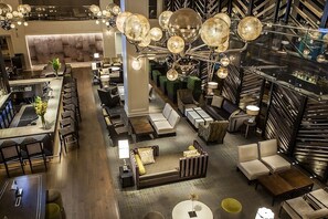 Eine großzügige Hotelhalle mit mehreren Sitzbereichen, einer Bar und einer Treppe.