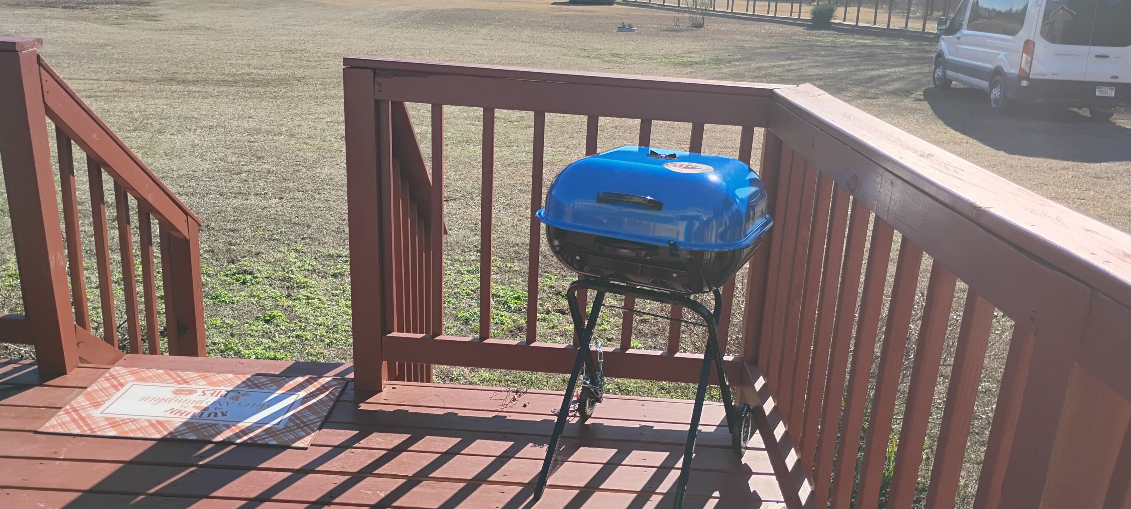 A blue grill on a wooden deck with a metal railing.
