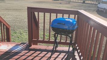 A blue grill on a wooden deck with a metal railing.