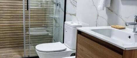A bathroom with a glass shower enclosure, two toilets, a sink, and wooden cabinetry.