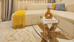 Una sala de estar con sofá, una mesita de centro de vidrio y una manta amarilla.