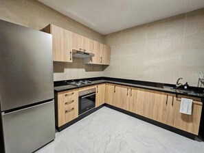 A kitchen with wooden cabinets, a stainless steel refrigerator, and a black countertop. - Modern 2-Bedroom Apartment – Near Downtown (Tanger)