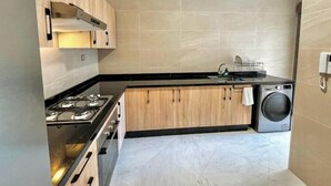 Cocina compacta con estufa a gas, armarios de madera, lavadora y salpicadero de azulejos.
