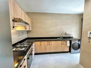 A compact kitchen with a gas stove, wooden cabinets, a washing machine, and a tiled backsplash. - Modern 2-Bedroom Apartment – Near Downtown (Tanger)