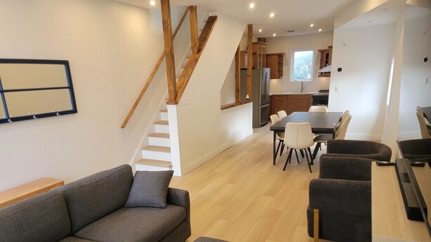 A modern living room with a sofa, ottoman, and dining area with chairs. A staircase leads to a kitchen with wooden cabinets and a refrigerator. - Stay in the heart of Toronto (toronto)