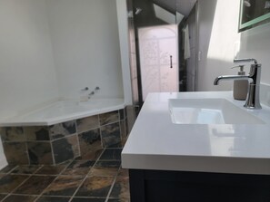 Une salle de bain avec un lavabo blanc, un robinet moderne et un espace douche doté d’un sol carrelé.