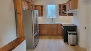 A compact kitchen with wooden cabinets, a stainless steel refrigerator, a sink, and a trash can. - Stay in the heart of Toronto (toronto)