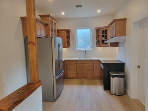 A compact kitchen with wooden cabinets, a stainless steel refrigerator, a sink, and a trash can. - Stay in the heart of Toronto (toronto)