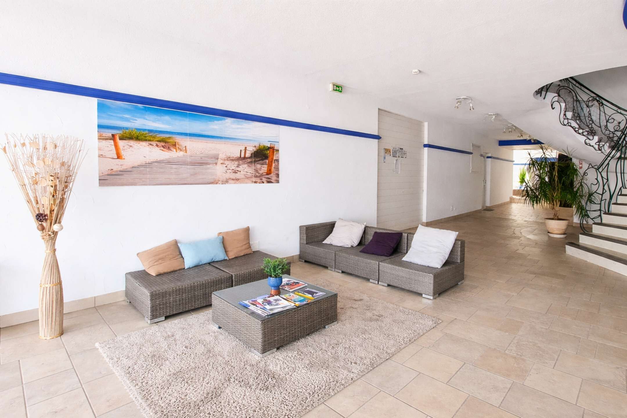 A lobby with wicker sofas, a coffee table, a large beach photo, and a staircase.