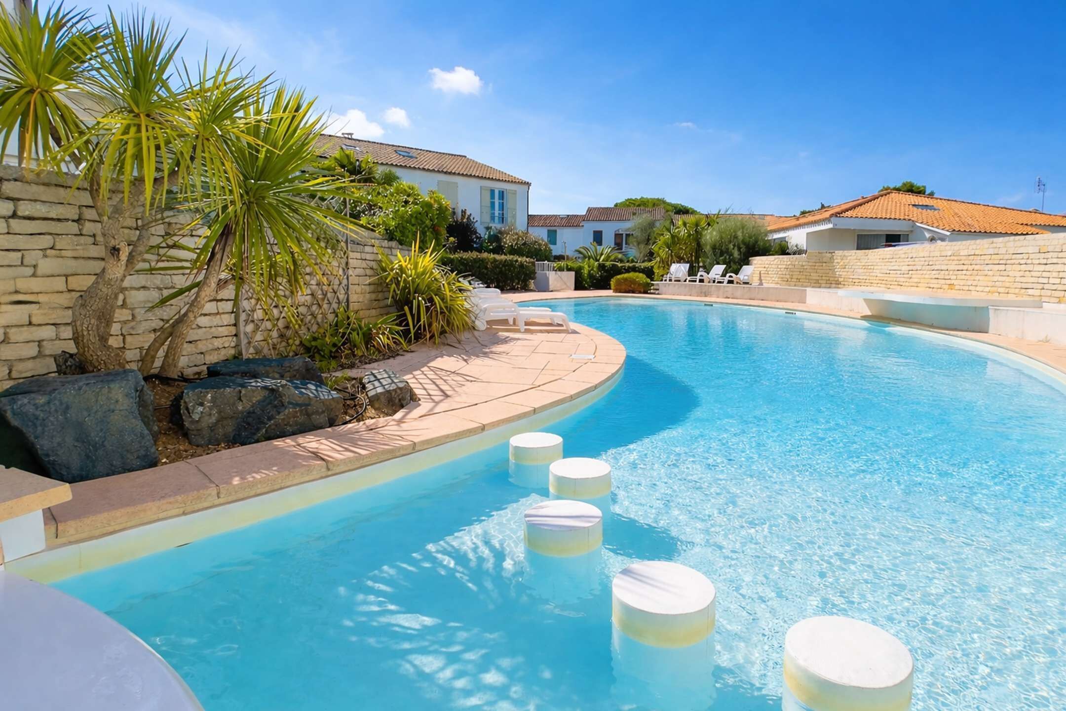 A swimming pool with a curved edge, surrounded by stone walls and palm trees.