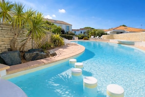 A swimming pool with a curved edge, surrounded by stone walls and palm trees. - Apartment with communal pool and parking (LA COUARDE SUR MER)