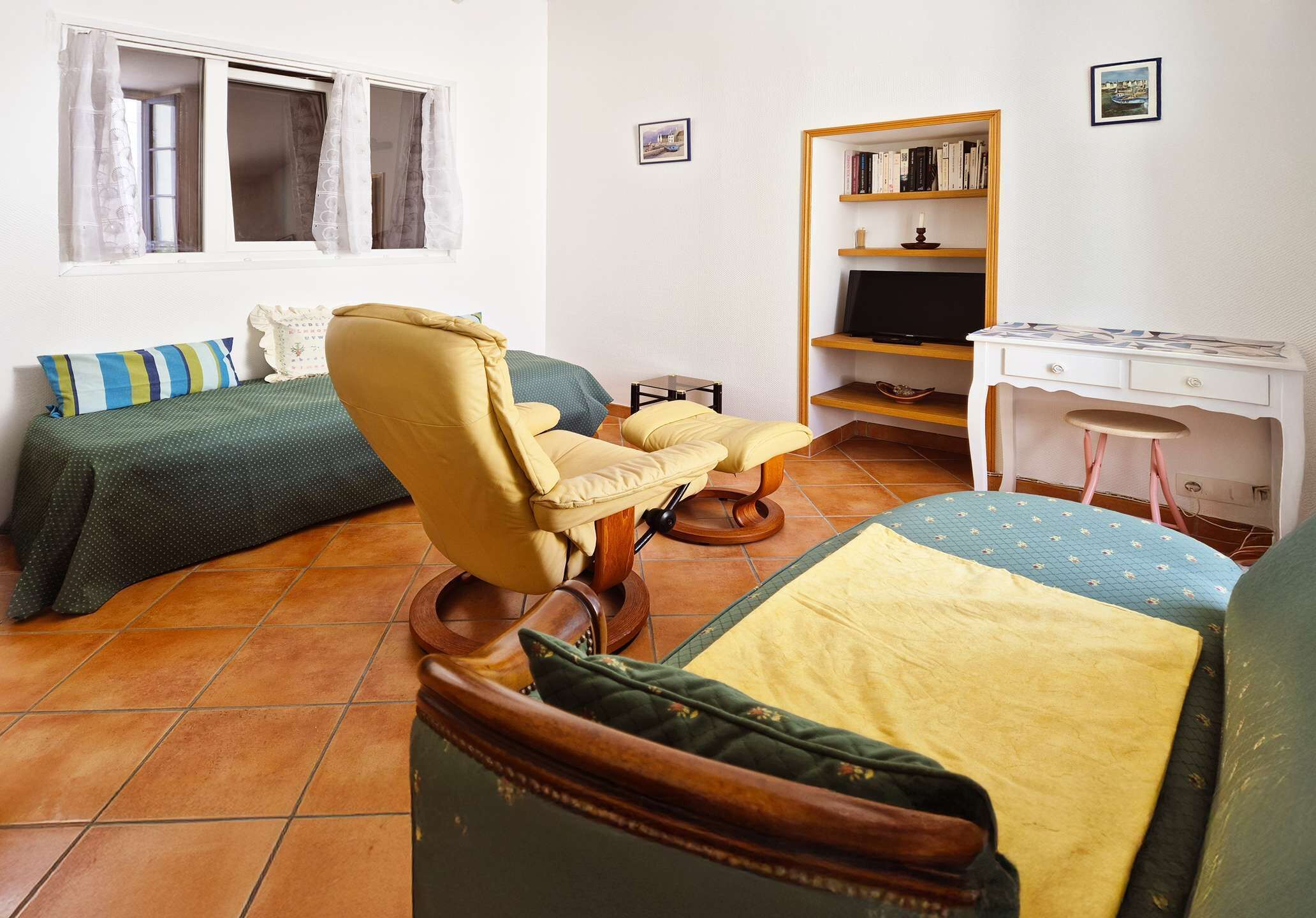 A room with a bed, a chair, a desk, a bookshelf, and a window.