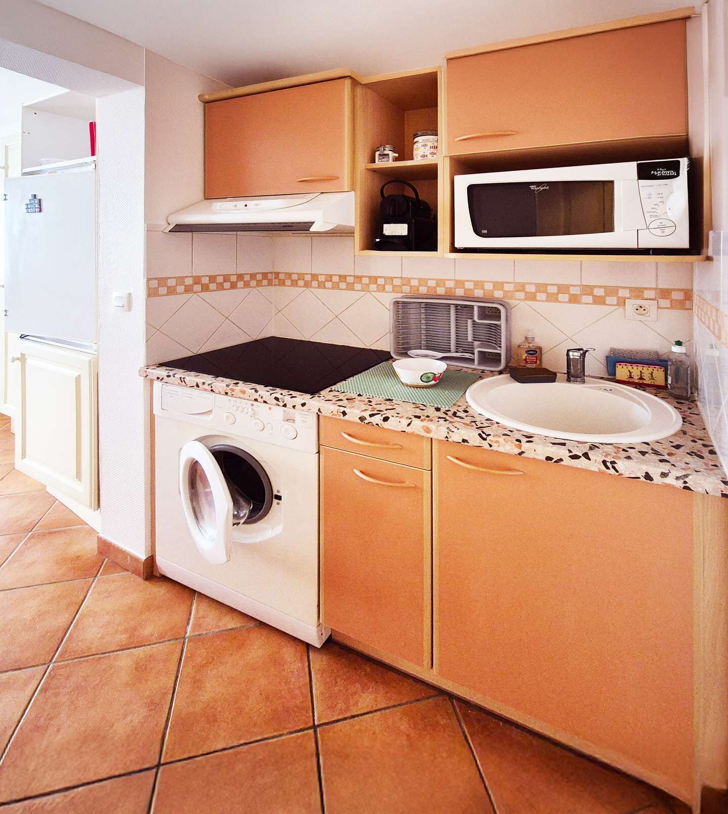 Een kleine keuken met een wasmachine, magnetron, spoelbak en betegelde achterwand.