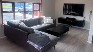 A modern living room with a sectional sofa, a flat-screen TV, and a large window with a view of a car and building.