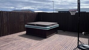 A rooftop deck with a hot tub, a basketball hoop, and a wooden floor.