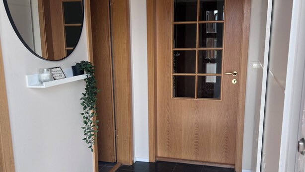 A hallway with a wooden door, a white shelf with a mirror, and a gray rug.