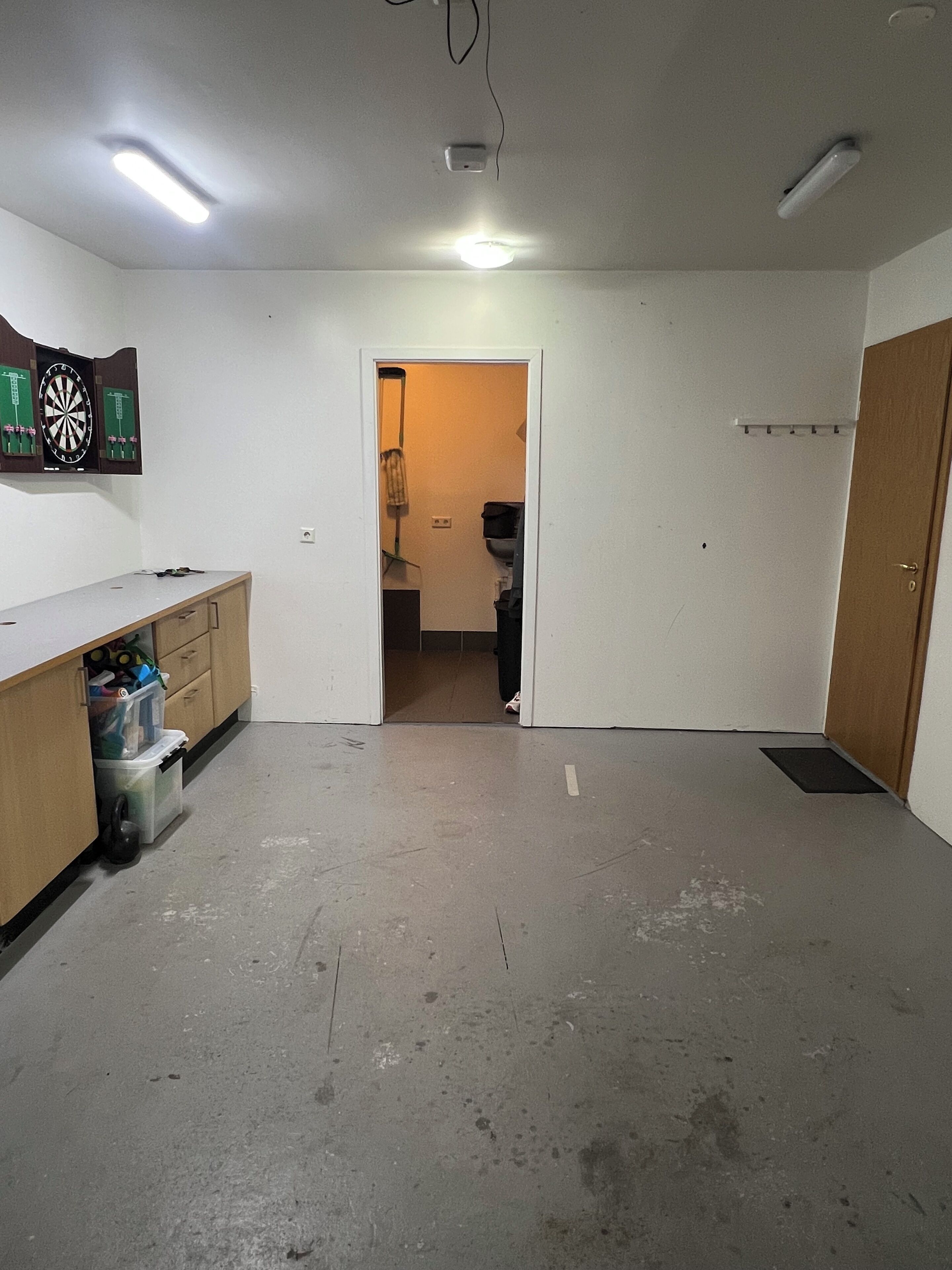 Ein Zimmer mit Dartscheibe, einem Holzschrank und einer Tür zu einem anderen Raum.