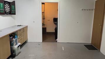 Ein Zimmer mit Dartscheibe, einem Holzschrank und einer Tür zu einem anderen Raum.