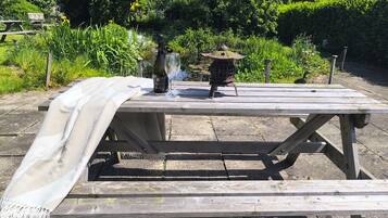 A wooden picnic table with a blanket, a bottle of wine, and a bird feeder.