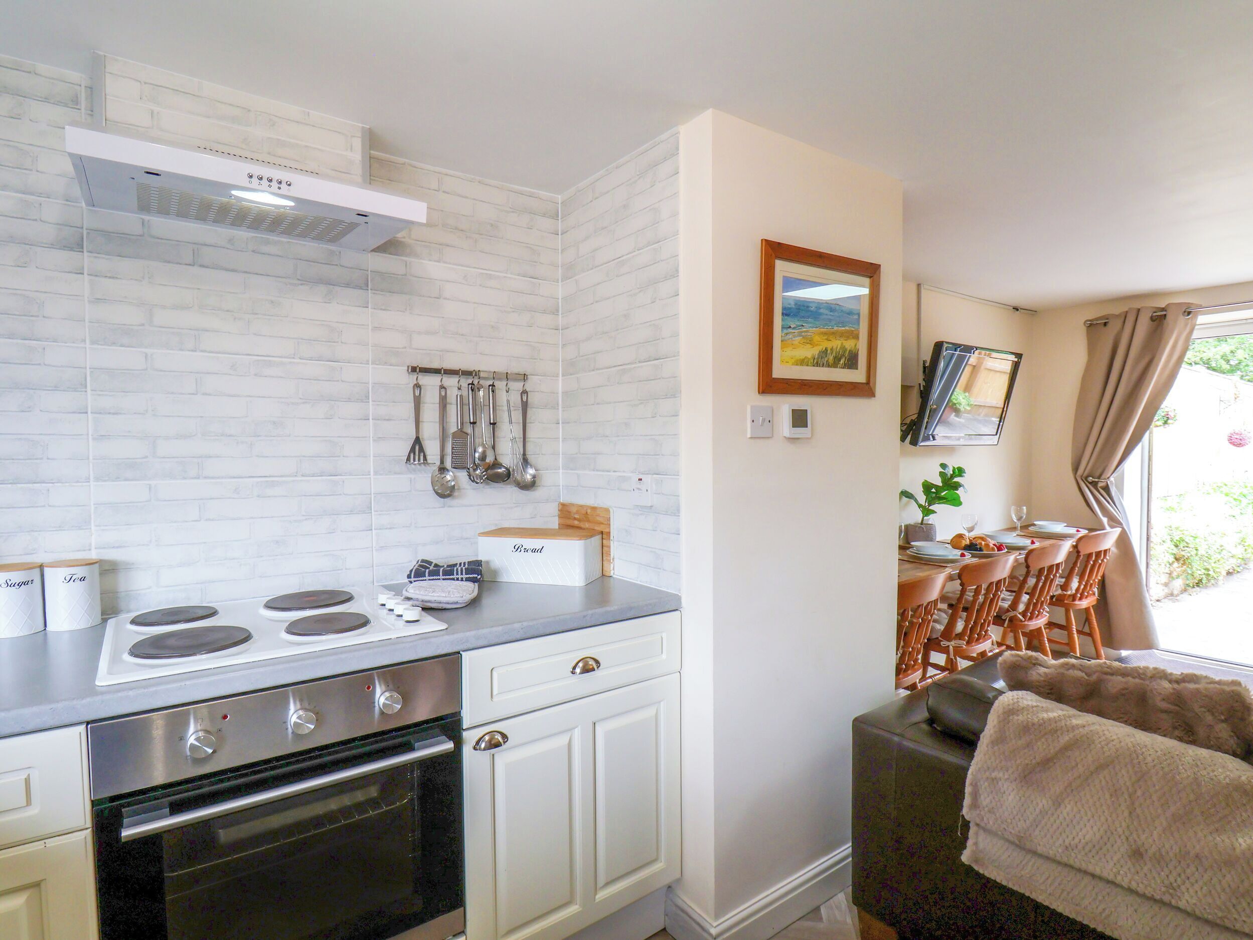 Cocina compacta con estufa, horno y muebles blancos. Cuenta con un comedor con mesa y sillas, y una ventana con cortinas.