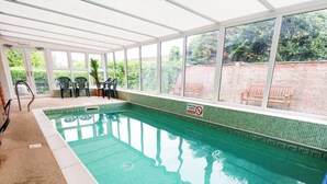 Ein überdachter Pool mit klarem Wasser, umgeben von einer Kachelwand und großen Fenstern.