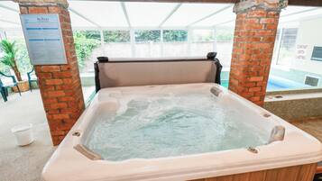 A hot tub under a wooden structure with brick pillars, a sign about spa pools, and a view of greenery outside.