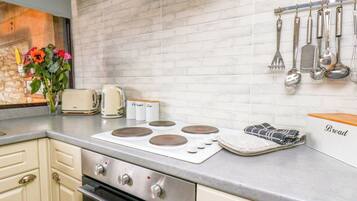 A kitchen with a white brick backsplash, a stove, oven, and a countertop with a tea kettle, sugar and tea containers, and a bread box.